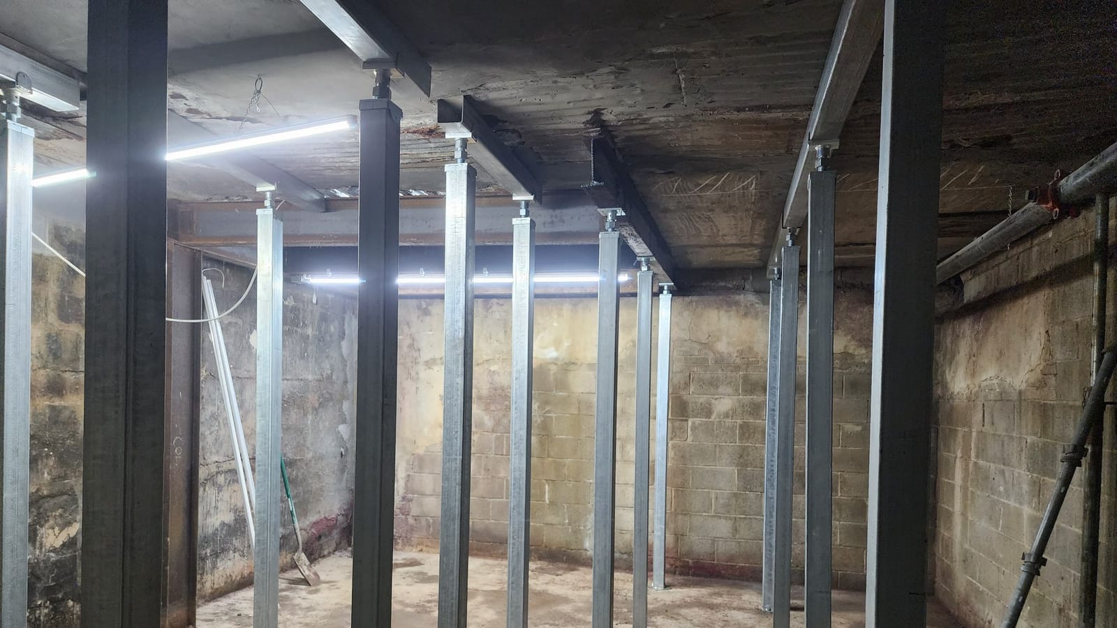 Temporary steel shoring supporting an existing concrete floor during structural work.